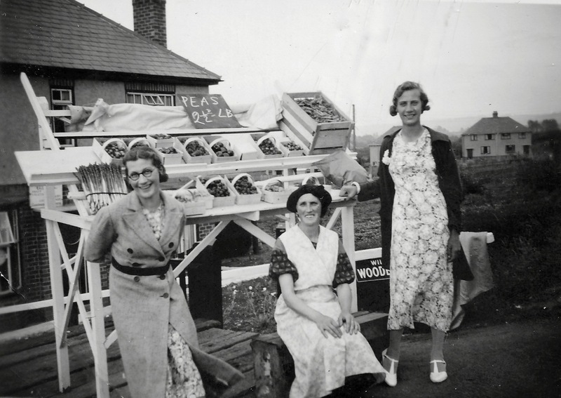 This stall was built by George Cox and put by the roadside next to his shop at 41 Pitchers Hill. By the stall, in 1938, are pictured his wife Dorothy and daughters Dorothy (Dot), with glasses, and Ruth.